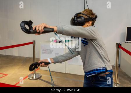 Acht Jahre Junge trägt VR-Headset, hält Controller in den Händen und genießen Sie neue Erfahrung in Videospielen. Spielstand auf der Messe der modernen tec Stockfoto