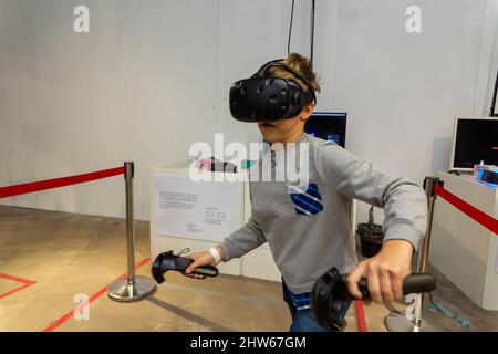 Acht Jahre Junge trägt VR-Headset, hält Controller in den Händen und genießen Sie neue Erfahrung in Videospielen. Spielstand auf der Messe der modernen tec Stockfoto