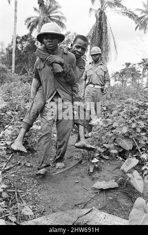 Ein biafranischer Soldat sah hier einen verletzten Kameraden während des Biafra-Konflikts tragen. 11.. Juni 1968. Der nigeranische Bürgerkrieg, auch bekannt als Biafrankrieg, dauerte zweieinhalb Jahre, vom 6. Juli 1967 bis zum 15. Januar 1970, und wurde gekämpft, um der Abspaltung von Biafra von Nigeria entgegenzuwirken. Die indigenen Igbo-Bewohner von Biafra fühlten sich nach der Unabhängigkeit von Großbritannien nicht mehr mit der nordeuropäischen Bundesregierung koexistieren können. Politische, wirtschaftliche, ethnische, kulturelle und religiöse Spannungen kochten schließlich nach dem Militärputsch von 1966 in einen Bürgerkrieg über, dann in einen Gegenkrieg Stockfoto