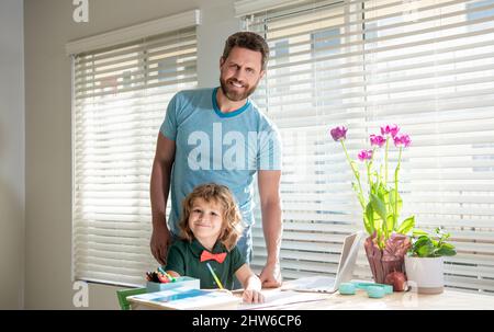 Glücklicher bärtiger Vater, der Schulaufgaben mit seinem Sohn im Klassenzimmer, zu Hause, geschrieben hat Stockfoto