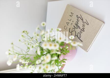 Vertikale Blumenaufnahme in einer rosa Vase und das Notizbuch mit inspirierendem Zitat auf dem weißen Tisch Stockfoto