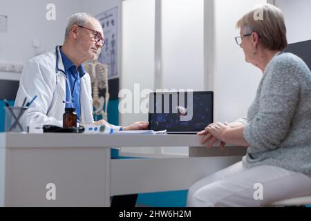 Medic zeigt die Illustration von Coronavirus-Bakterien auf dem Laptop für den Patienten im Schrank. Medizinischer Spezialist und Patient, der auf den Computerbildschirm schaut, mit visueller Darstellung der covid 19 Pandemie. Stockfoto