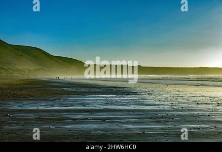 Blick zurück entlang Rhossili Beach in Richtung Rhossili mit nassem Sand an einem Januartag bei Sonnenschein Stockfoto