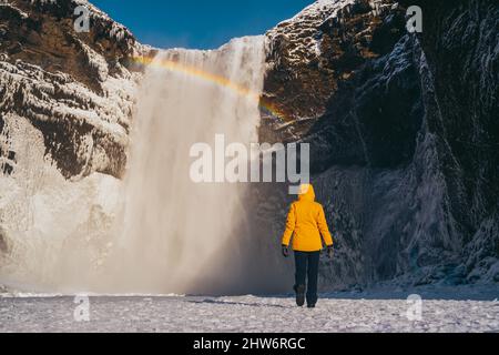 Spanische Frau mit gelbem Mantel am skogafoss Wasserfall Stockfoto