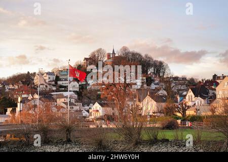 Blankenese in der Stadt Hamburg, Deutschland. Wohlhabende Nachbarschaft. Sonnenuntergang Stadtbild Blick mit Süllberg, berühmten Hügel in Blankenese und Flagge von Hamburg. Stockfoto