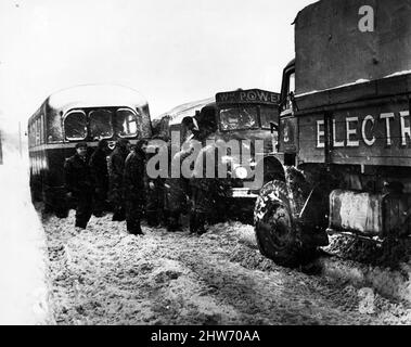 Eine Gruppe von Männern, die bei einem Schneesturm auf der Straße zwischen Cwmbran und Pontypool einen Lastwagen und Bus herausziehen, der im dichten Schnee feststecken geblieben ist.Januar 1963. Stockfoto