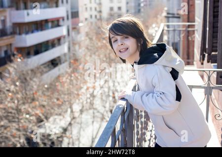 Kind, stehend auf einem Balkon in einer Wohnung in Barcelona, genießen Sonne und schönes Winterwetter, Spanien Stockfoto