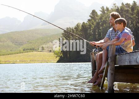 Cast Aways. Aufnahme eines Vaters und eines Sohnes, der auf einem Steg sitzt und zusammen fischt. Stockfoto