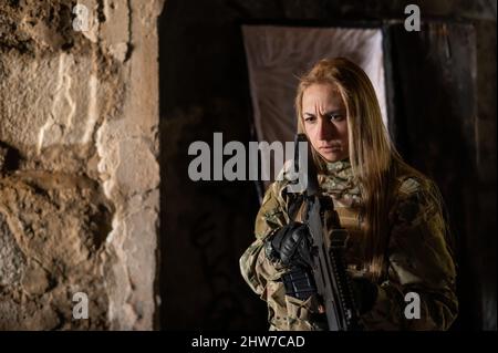 Kaukasische Frau in Armeeuniform, die ein Maschinengewehr hält und in der Nähe eines offenen Sarges steht. Stockfoto