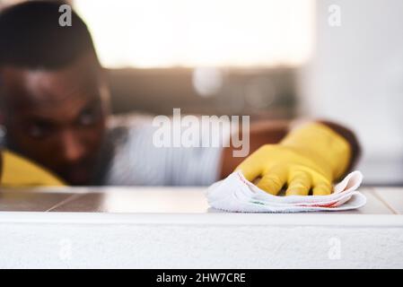 Ich bevorzuge es, dass mein Zuhause makellos ist. Eine kurze Aufnahme eines unkenntlichen Mannes, der zu Hause eine Küchentheke putzt. Stockfoto