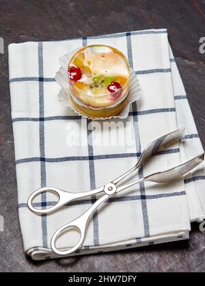 Kuchen mit Gelee, Kiwi, Kirschen und Mango auf dem Tisch. Leckeres Mini-Dessert auf einem hölzernen Hintergrund, Nahaufnahme. Stockfoto