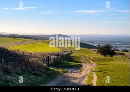 Weit reichende Ausblicke über die Sussex-Landschaft bei Sonnenschein im Februar mit Menschen, die auf dem South Downs Way in der Nähe von Ditchling Beacon in East Sussex, England, wandern. Stockfoto