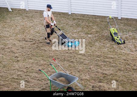 Der Mensch-Gärtner, der Rasen mit einem Vertikutierer erscharft, erscharft den Rasen und entfernt altes Gras Stockfoto