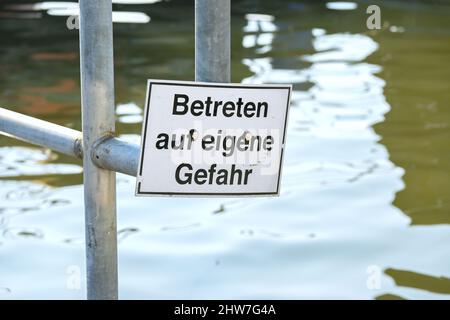 Warnschild am Kaikante im Hafen mit deutschem Text, Bedeutung: Auf eigene Gefahr eingeben, Platz im Wasser kopieren, ausgewählter Fokus, enge Tiefe von f Stockfoto