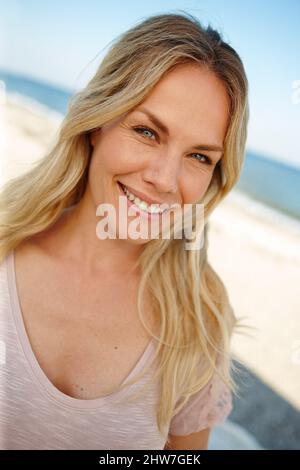 Der perfekte Ort, um dem ganzen zu entfliehen. Kopf- und Schulterporträt einer attraktiven jungen Frau, die an einem sonnigen Strand steht. Stockfoto