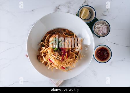 Nördliche thailändische khao Soi Chicken-Kurvennudeln in einem Gericht isoliert auf matter Draufsicht auf grauem Marmorboden Stockfoto