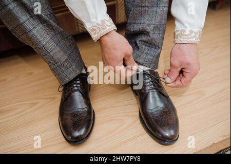 Der Typ bindet die Schnürsenkel auf schwarzen klassischen Schuhen. Der Bräutigam trägt schöne Schuhe und bindet seine Schnürsenkel Stockfoto