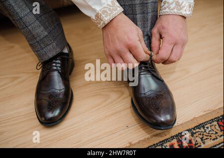 Der Typ bindet die Schnürsenkel auf schwarzen klassischen Schuhen. Der Bräutigam trägt schöne Schuhe und bindet seine Schnürsenkel Stockfoto