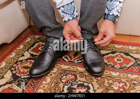 Der Typ bindet die Schnürsenkel auf schwarzen klassischen Schuhen. Der Bräutigam trägt schöne Schuhe und bindet seine Schnürsenkel Stockfoto