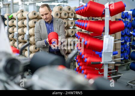 01. März 2022, Sachsen, Flöha: Nico Teutsch, Geschäftsführer, kontrolliert Garne in der Wickelabteilung der OTEX Textilveredlung GmbH. Das Unternehmen mit 90 Mitarbeitern produziert Spezialgarne für Medizinprodukte und technische Textilien. Bei der Suche nach einem Nachfolger für das Werk im Jahr 2016 übernahm die Thüringer Bauerfeind AG, ein Hersteller von medizinischen Hilfsmitteln wie Verbänden, Orthesen oder orthopädischen Einlagen, einfach den Lieferanten selbst. Die Zahl der Beschäftigten stieg, und nun gehören auch mehrere Rumänen und Südamerikaner zur Belegschaft. Foto: Jan Woitas/dpa-Zentralbild/ZB Stockfoto