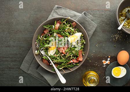 Frischer Dandelion-Salat mit Speck und Eiern auf grauem Hintergrund Stockfoto