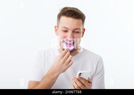 Ein Mann hält in der Hand eine ultraviolette Lampe für die Zahnaufhellung zu Hause. Ein schneeweißes Lächeln nach dem Bleichen. Stockfoto