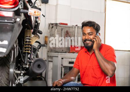 Lächelnder Mechaniker, der im Ausstellungsraum mit dem Kunden über Reparatur oder Wartung telefoniert - Konzept glücklich über Kundenservice, Entspannung und Stockfoto