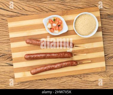 Schweinewurstspieße über Holzbrett mit Farofa und Vinaigrette. Stockfoto