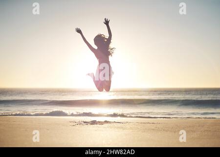 Freiheit liegt in der Kühnheit. Aufnahme einer jungen Frau, die am Strand in die Luft springt. Stockfoto