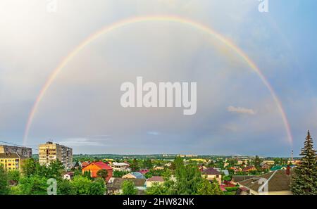 Panoramafoto eines Regenbogens am Himmel über einer kleinen Stadt Stockfoto