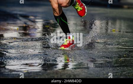 Die Beine der Läufer in Kompressionssocken laufen in einer Pfütze, die Wasser spritzt Stockfoto