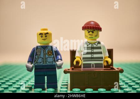 Nahaufnahme einer Lego-Polizist-Spielzeugfigur, die neben einem Gefangenen in einer Schatzkiste steht. Stockfoto