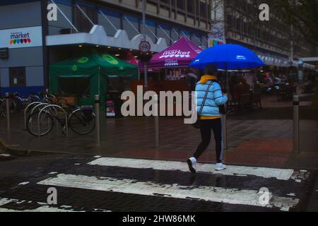 Alltagsleben - Rückansicht einer jungen Frau, die sich beim Überqueren der Straßenkreuzung, Chelmsford City Center Market, Essex, Großbritannien, brüllig klammert. Stockfoto