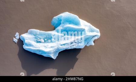 Blick von oben auf einen blauen Eisberg in der Fjallsarlon-Gletscherlagune im Süden Islands. Das umgebende Wasser ist aufgrund vulkanischer Schlammablagerungen braun. Dro Stockfoto