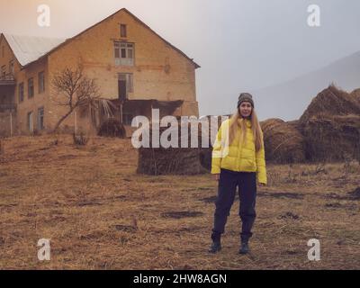 Frau auf dem Land unter gerollten Heuhaufen vor dem Hintergrund eines alten leeren Gebäudes an einem nebligen Herbsttag Stockfoto