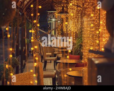 Ein gemütliches, leeres Café in der Abendbeleuchtung vieler Girlanden auf der Veranda. Weichfokus Stockfoto