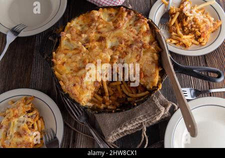 Rustikaler Pasta-Auflauf, der in einer gusseisernen Pfanne gebacken und auf einem Holztisch serviert wird. Ansicht von oben Stockfoto