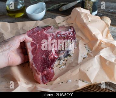 Frau´s Hand hält ein großes Steak in der Hand. Frisches und organisches Porterhouse auf Metzgerpapier Stockfoto