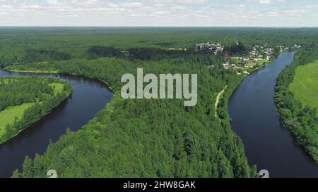 Draufsicht auf grünen Wald mit Flüssen und Dorf am Hintergrund Horizont mit blauem Himmel. Aufnahme. Schöne Sommerlandschaft mit grünem Wald und blauem Drive Stockfoto