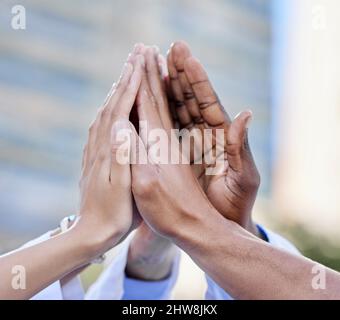 Mit Teamwork können wir alles erreichen. Aufnahme einer Gruppe von nicht erkennbaren Ärzten, die sich gegenseitig eine hohe fünf vor einem Stadthintergrund geben. Stockfoto
