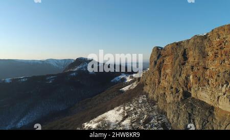 Landschaft von schneebedeckten Klippen an einem suny Tag auf blauem Himmel Hintergrund. Luftaufnahme der steilen Klippen und grünen dichten Wald an ihren Hängen und Stockfoto