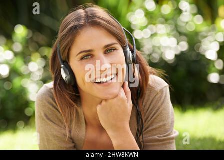 Genießen Sie die Symphonie der Natur. Aufnahme einer wunderschönen jungen Frau, die im Freien liegt und Musik hört. Stockfoto