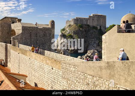 Altstadt von Dubrovnik, Kroatien - Touristen, die entlang der alten Stadtmauer spazieren und die Festung Lovrijenac sehen Stockfoto