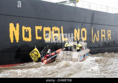 Wedel, Deutschland. 04. März 2022. Aktivisten von Greenpeace fahren auf der Elbe zwischen Wedel (Schleswig-Holstein) und Hamburg in einem Schlauchboot, um den Kohlefrachter "Grand T", der auf dem Weg zum Hamburger Hafen mit russischer Kohle beladen ist, mit dem Slogan "No Coal no war" zu besetzen. Und werden von einem Polizeiboot weggeschoben. Quelle: Daniel Bockwoldt/dpa/Alamy Live News Stockfoto