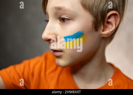 Ein überraschendes Kind gegen den Krieg, mit einer gemalten Flagge der Ukraine auf seinen Wangen Stockfoto