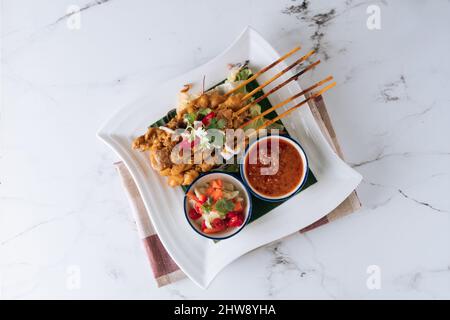Traditionelle malaysische Hähnchen-Satay-Spieße mit Chilisauce und Salat in einem Gericht, das auf matter Draufsicht auf grauem Marmorboden isoliert ist Stockfoto