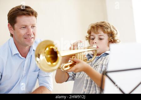 Stolz auf seinen kleinen Trompeter. Aufnahme eines niedlichen kleinen Jungen, der die Trompete spielt, während sein Vater ihm stolz zuschaut. Stockfoto