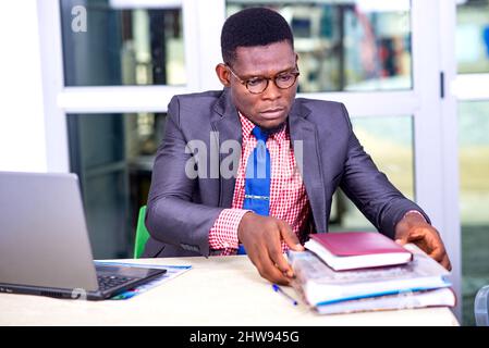 Gutaussehender Geschäftsmann in Jacke, der seine Akten auf seinem Schreibtisch arrangiert. Stockfoto