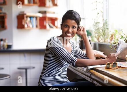 Mit ihrem Kaffee einige Neuigkeiten einzufangen. Eine junge Frau, die in einem Café mit einer Zeitung in der Hand sitzt. Stockfoto