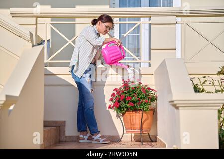 Gartenarbeit von Balkon, Terrasse, Veranda, Frau wässert blühenden Pflanzen aus Gießkannen Stockfoto